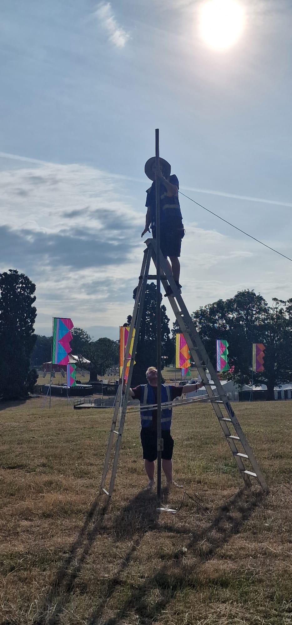 Two HTG engineers raising a mast at Deershed Festival 2026 with the stage and festival flags in the background